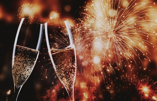 toasting with champagne glasses against holiday lights and new year fireworks