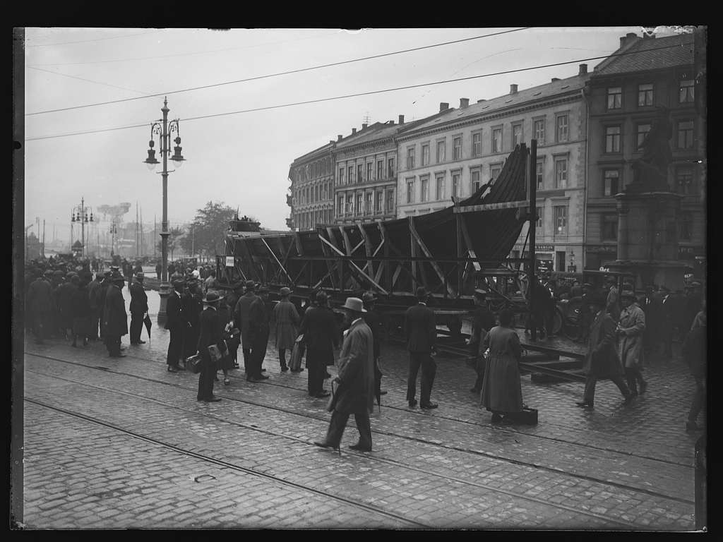 ship in wooden supports on rails on city streets surrounded by people in suits