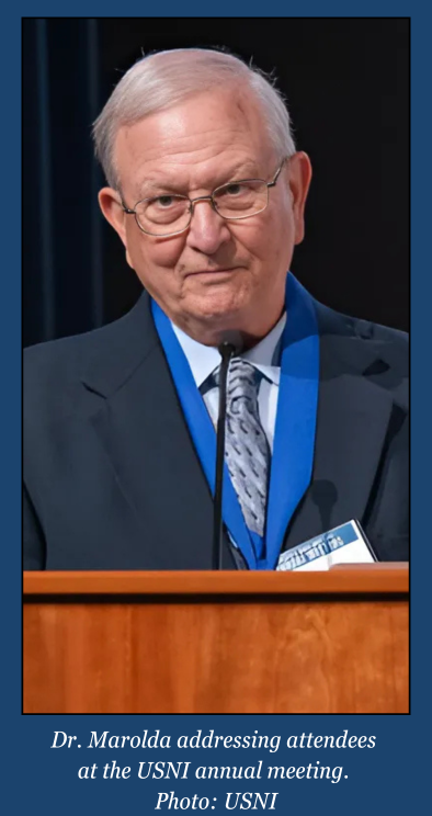 Dr. Edward Marolda speaks at a podium during the USNI annual meeting, wearing a suit and medal. (Photo courtesy of USNI)