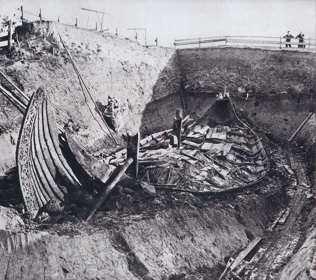 dig site with boat steam and stern rising up at each end of field of pieces of wood in boat shape