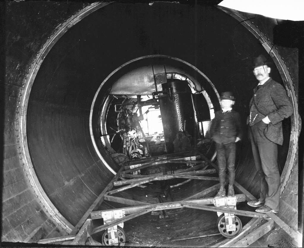 A man and a boy stand inside a roller boat cylinder 