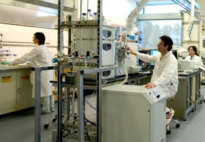 three scientists in white lab coats operating equipment in a lab