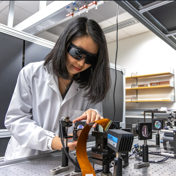 engineer in white lab coat working on hardware optical equipment in lab