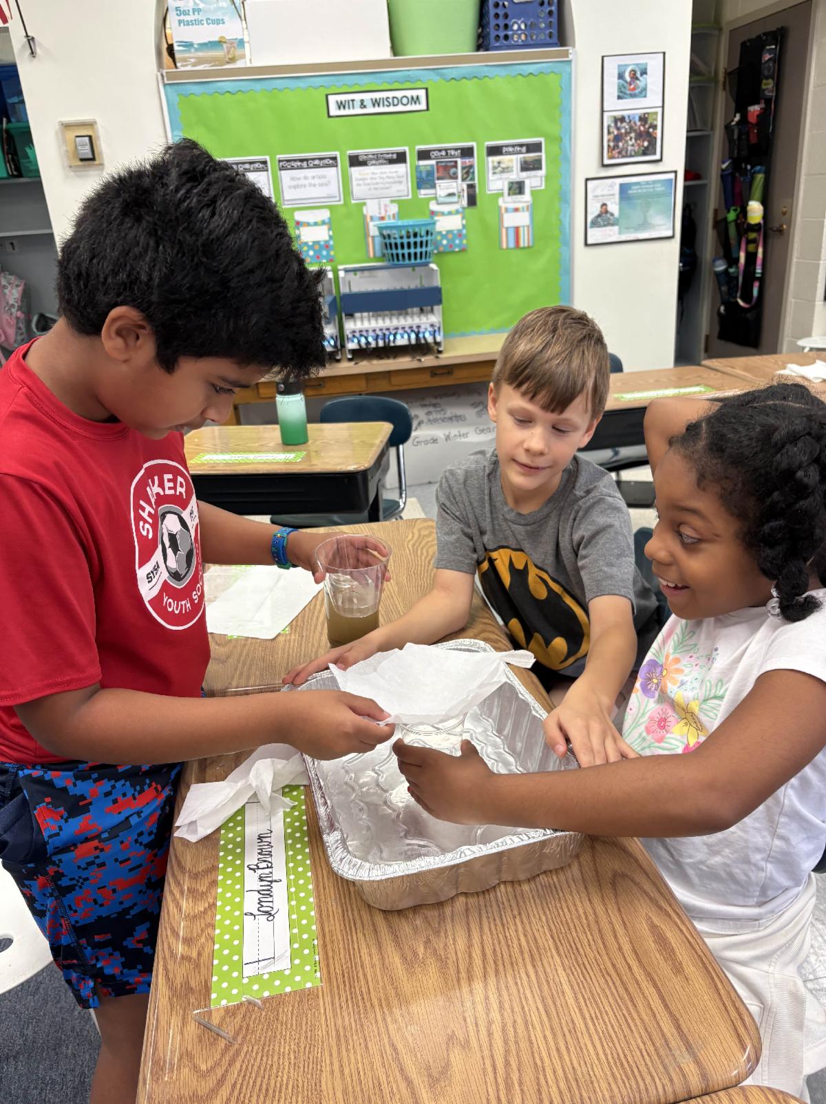 Three students sit at a table and use a water filter they created.
