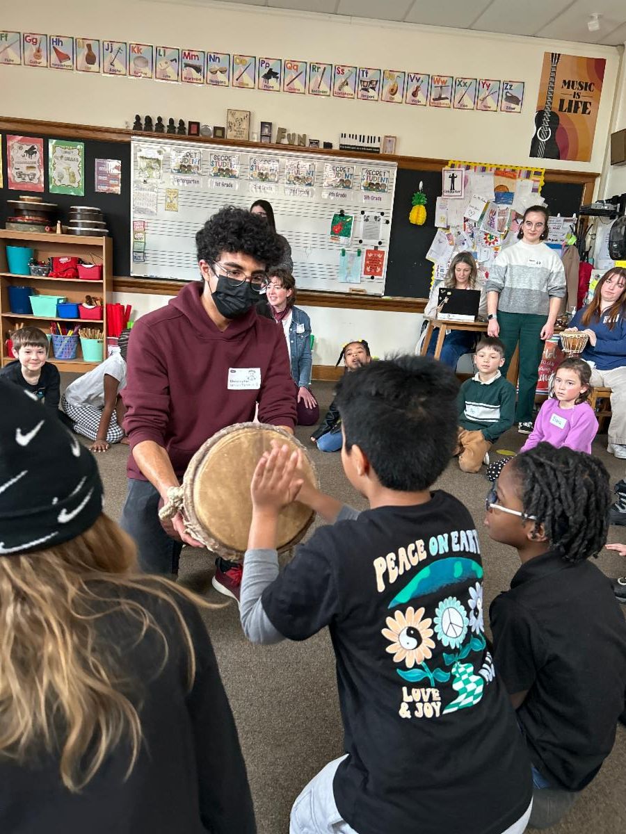 A student in Christine Fader's class at Onaway plays on a drum, which is held by a student from Case Western Reserve University.