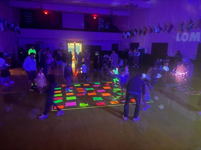 Students and their parents dance in a dark room with neon lights during Lomond's Sneaker Ball.
