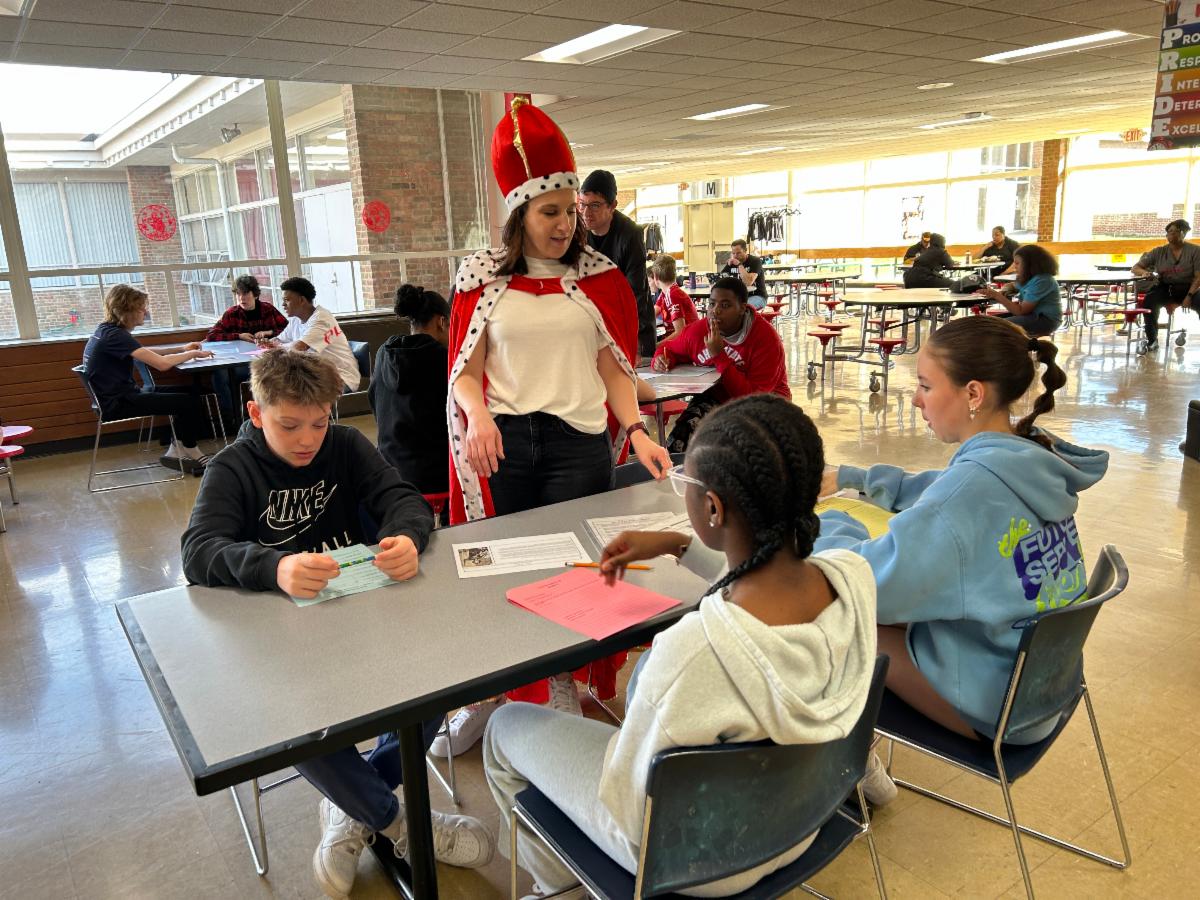 Individuals & Societies Teacher Sarah Knebel wears a red cape and king's crown while speaking to Grade 7 students during the Renaissance Faire.