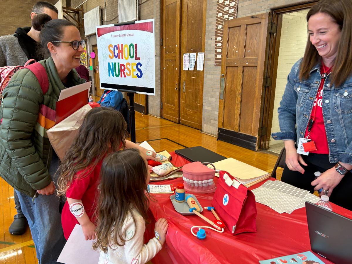 Students and parents talk to a school nurse and play with toys on the table during Kindergarten Kickoff.