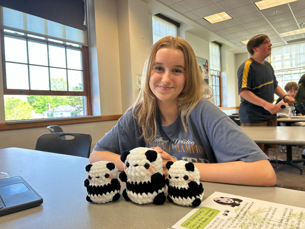 A Grade 10 student sits at a table with three crocheted pandas for her Personal Project.