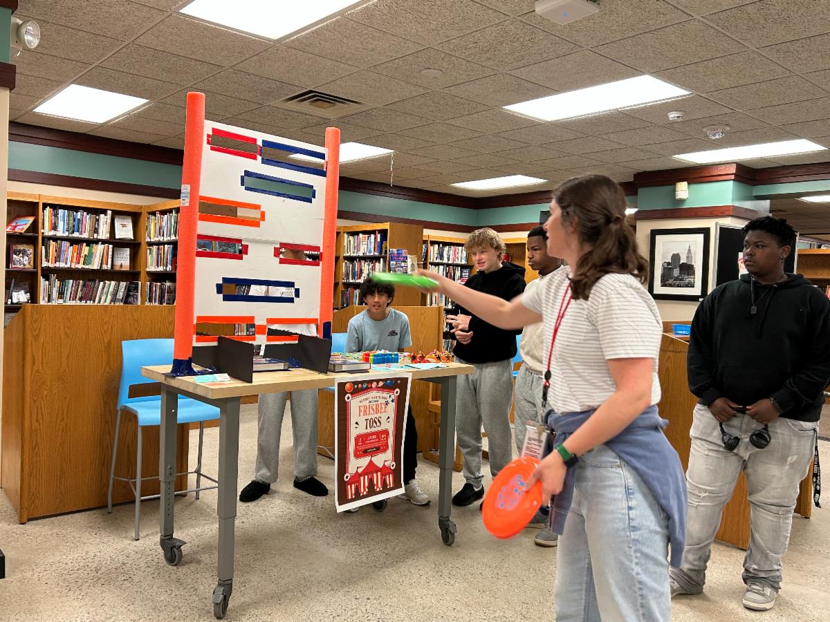 A student throws a frisbee into a slot in a board as part of the Geometry Carnival held in the SHHS Library.