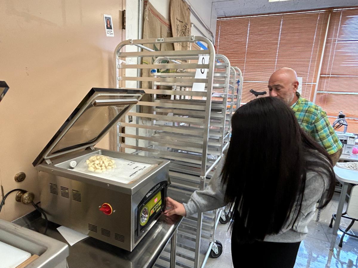 A student places a bag of garlic in a vacuum sealer machine.