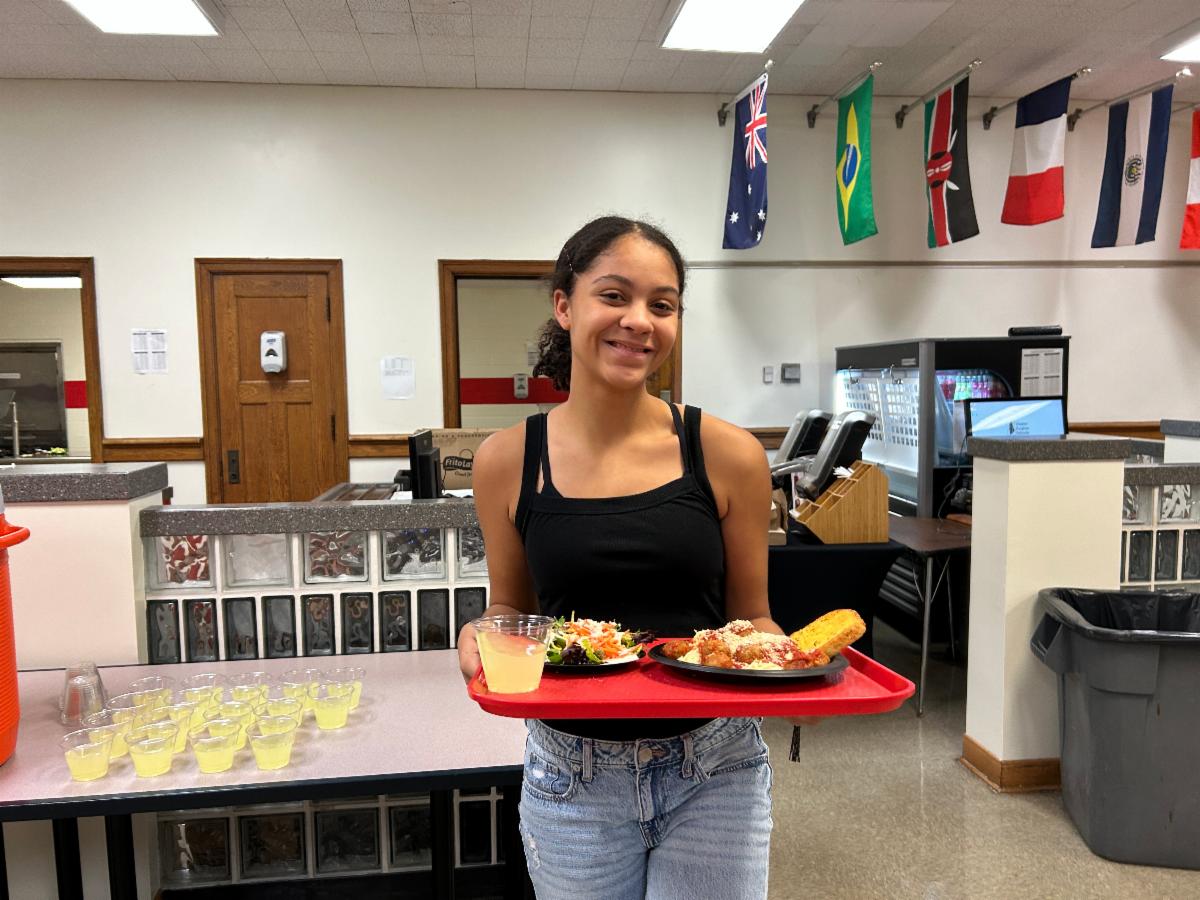 A SHHS student who is a member of YEH holds a tray of spaghetti.