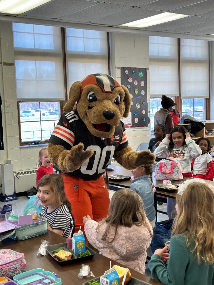 Chomps, a dog-like mascot wearing a Cleveland Browns uniform, visits with Onaway Kindergarten students in the cafeteria.