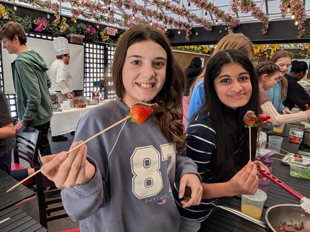 Two Middle School French students smile and hold chocolate covered strawberries.