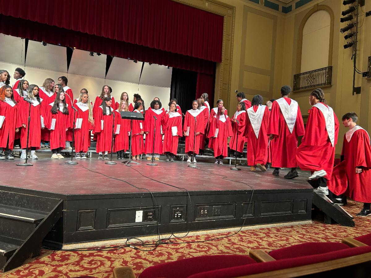 The combined men's and women's choir walks onto the stage.