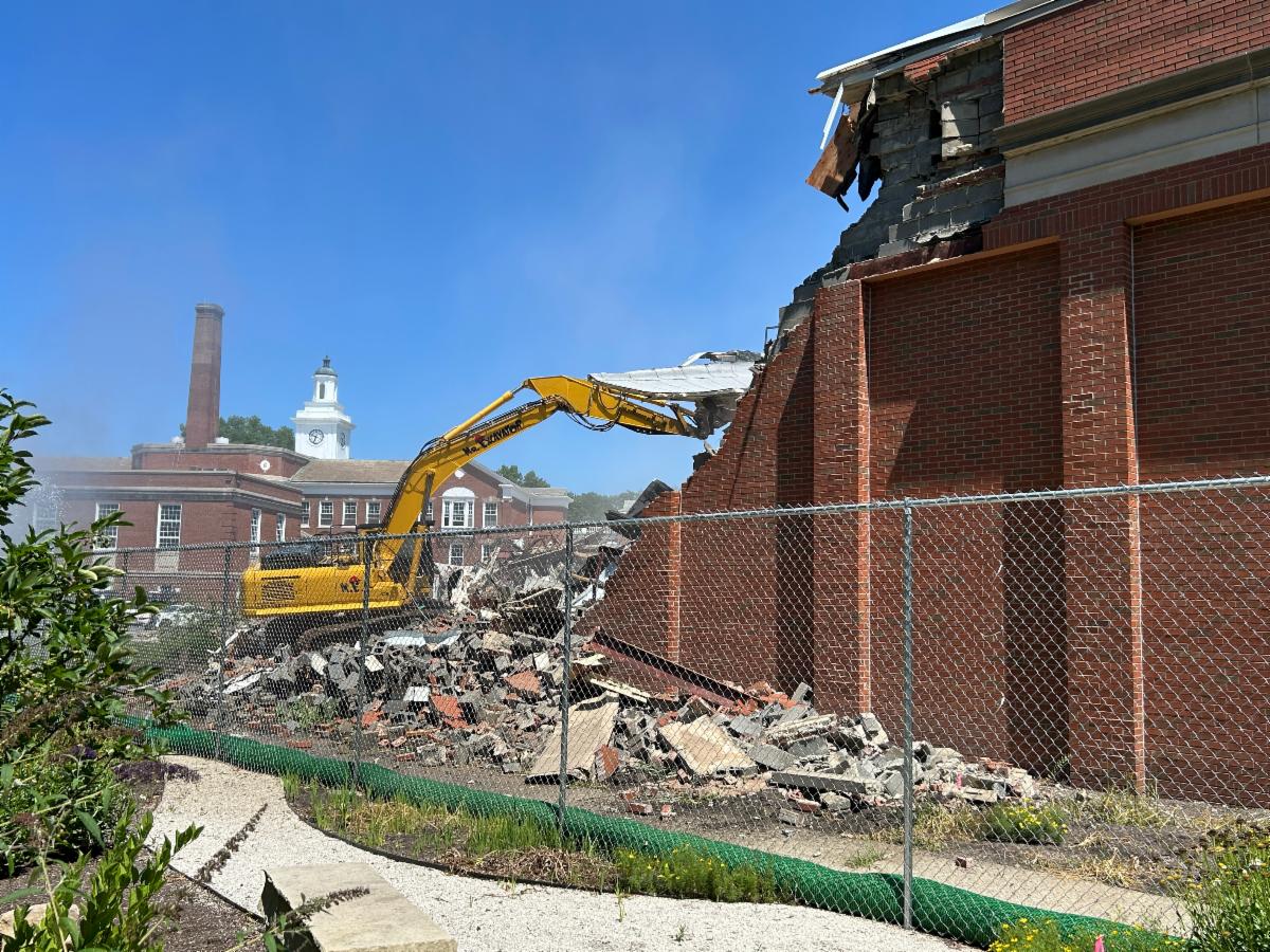 An excavator tears down the pool at the former Woodbury Elementary School and there is a pile of rubble in the foreground.