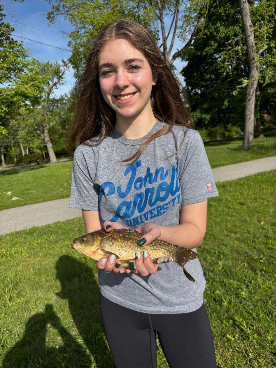 A SHHS student stands in the grass holding a fish she caught.