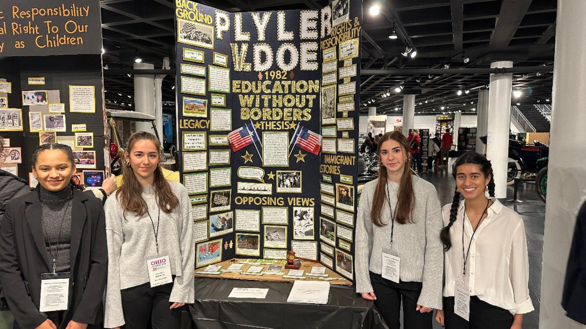 Four students stand in front of a trifold board on "Plyler v. Doe" during the National History Day competition.