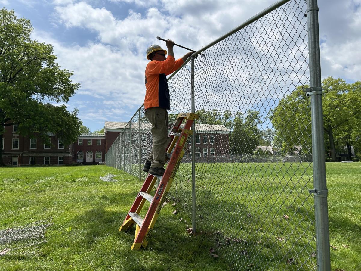 A contractor stands on a ladder while putting up fencing around Woodbury.
