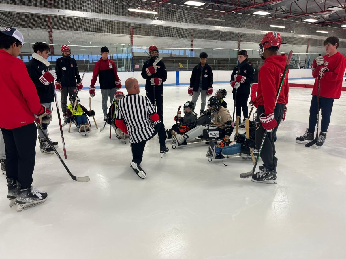 SHHS hockey players and Youth Challenge players gather around a referee on the ice.