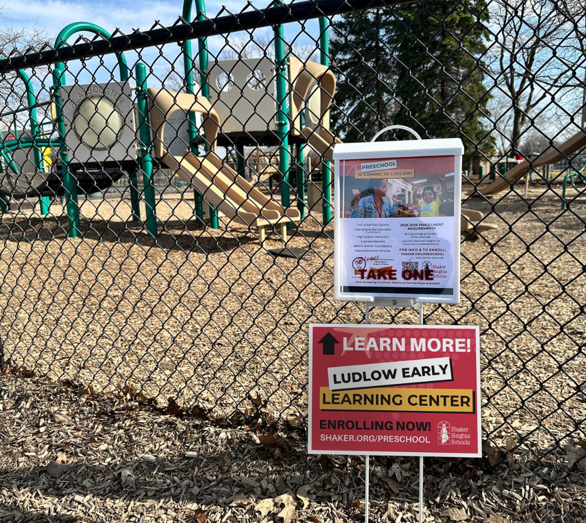 This is a picture of a white flyer box at the Onaway playground. The flyer box has flyers inside for the Ludlow Early Learning Center.