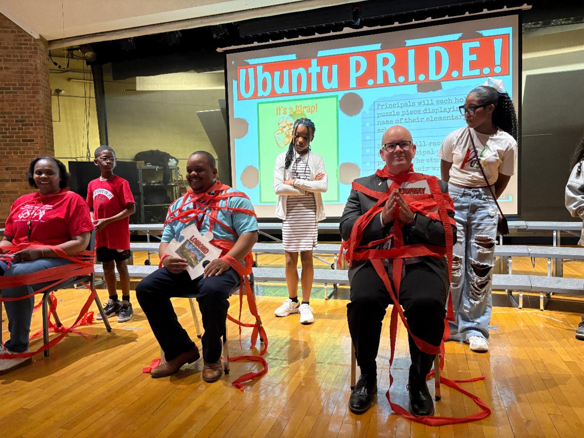 Elementary Principals Roneisha Campbell, George Clark and Chris Hayward sit on the stage at SHMS wrapped in red ribbon during the pep rally.