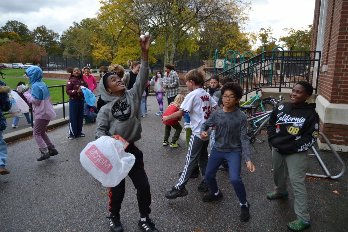 An Onaway student holds an egg in the air while standing outside on the blacktop.