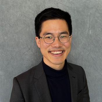 Man with glasses wearing a black shirt and blazer.