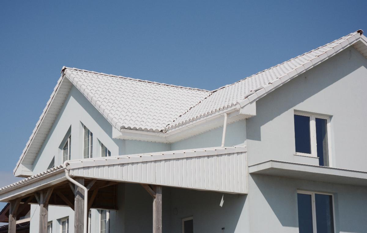 A white house with white roof shingles. A blue sky is overhead.