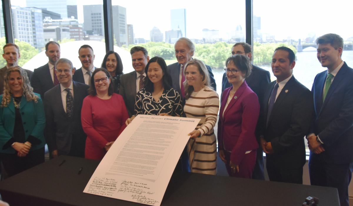 Mayors from the Metro Mayors Coalition along with some MAPC staff stand together behind the large signed Climate Commitment poster.