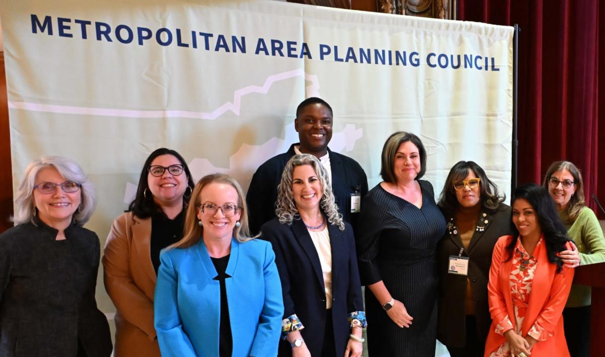 A group of nine people pose for a photo in front of a large Metropolitan Area Planning Council banner.