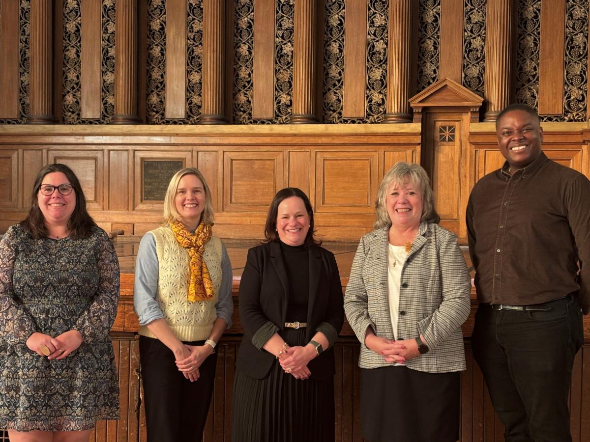 Five people stand side by side in front of a carved wooden wall inside Melrose Memorial Hall.