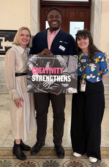 Three people smiling and standing together indoors, holding a poster that reads “Creativity Strengthens.” From left to right: Dr. Annis Sengupta in a white polka dot dress, Lafayette Cruise in a navy blazer and pink shirt, and Abbey Judd in a colorful floral shirt with black pants.