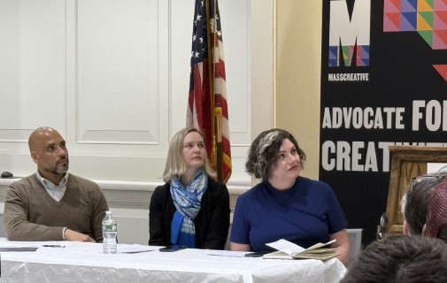 Three panelists sit at a table with an American flag and a 'MASSCREATIVE' banner behind them.&nbsp;