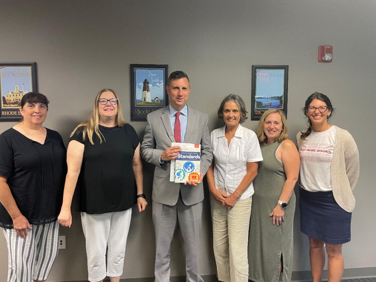 Esther Wolk, Deanna Brooks, Mary Moen, Melanie Roy, and Tasha White present Congressman Seth Magaziner with a copy of the AASL standards. 