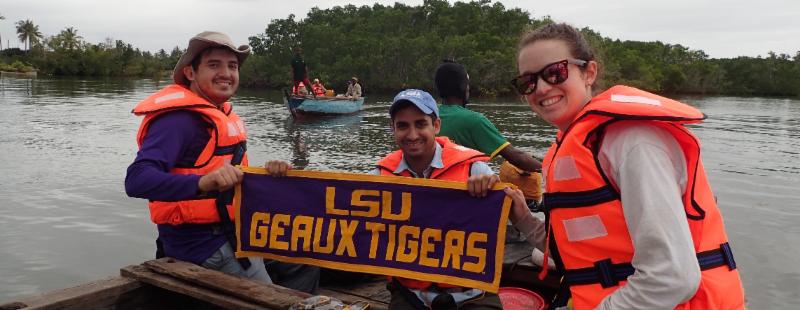 Mario Hernandez and two other researchers on a boat holding a banner that reads: LSU Geaux Tigers.
