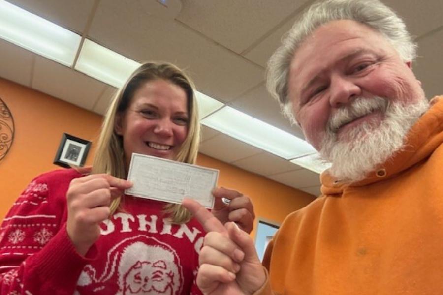 Tabitha and Brady stand together Tabitha is holding a donation check and Brady the donor is pointing to it.