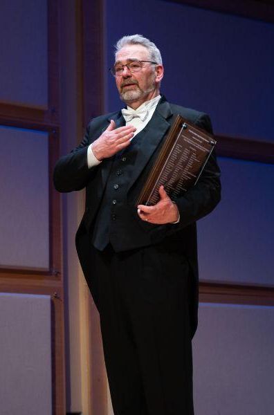 Anderson stands ontage with his hand on his heart and holds a plaque
