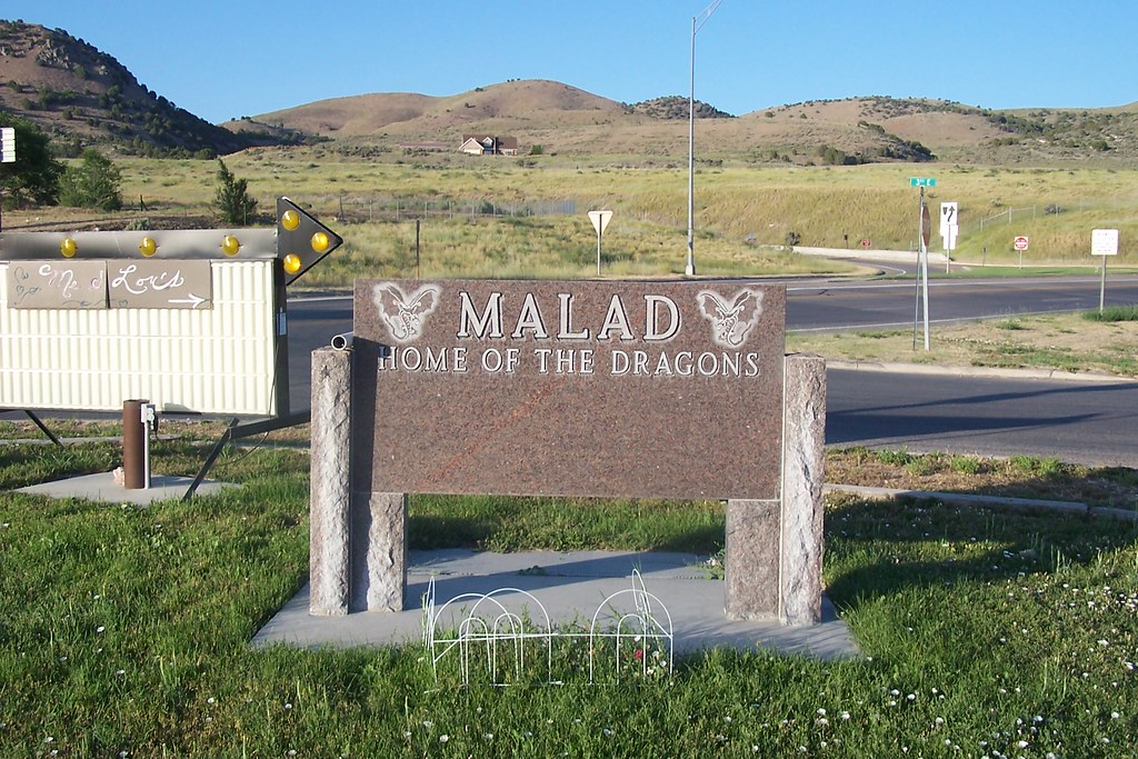 Sign that says Malad, home of the dragons, with hills and blue sky in background