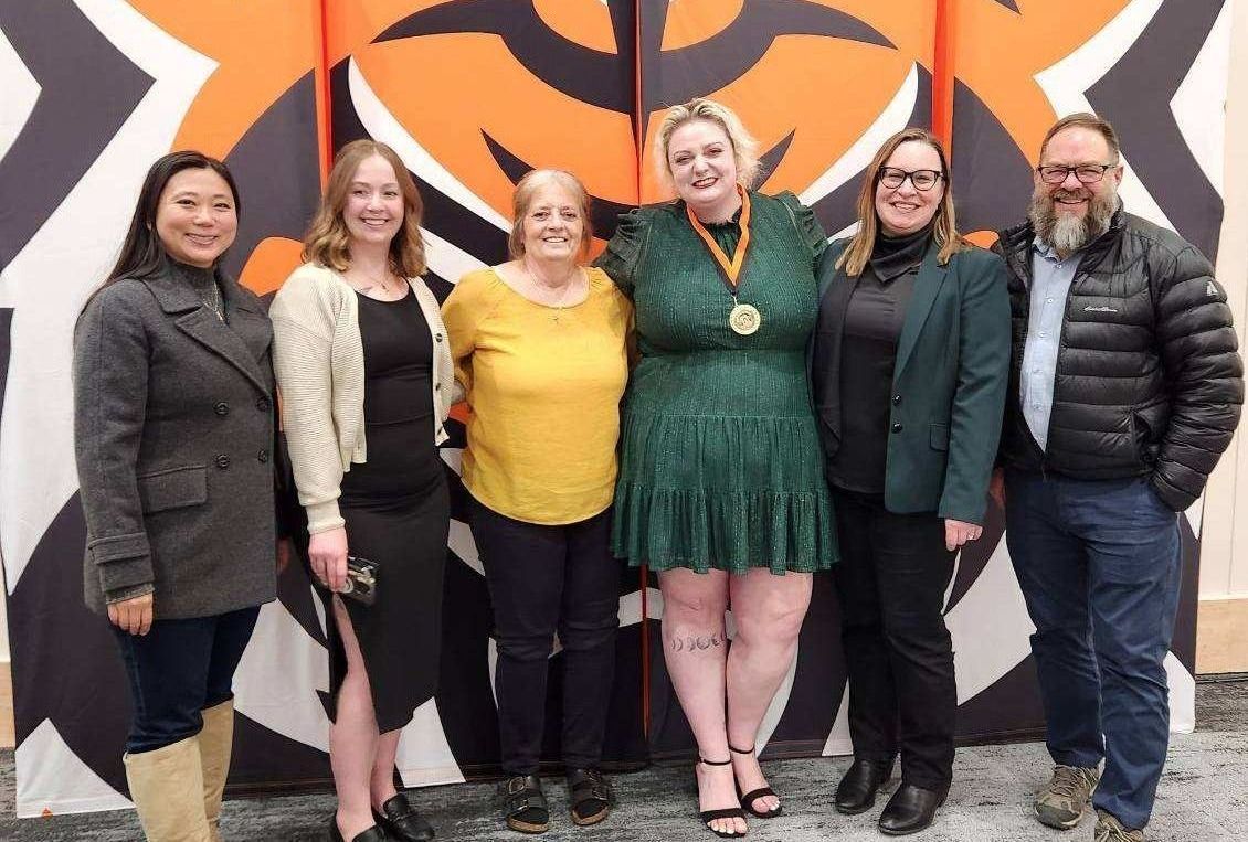 Award recipients and faculty and loved ones post together for a group photo in front of a graphic of the Bengal Head logo at the awards ceremony