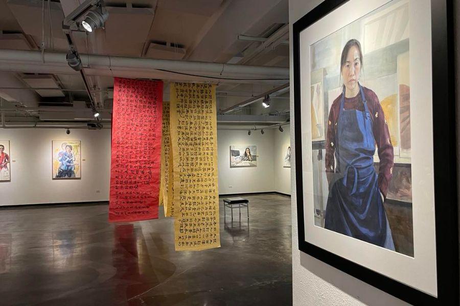 A watercolor self-portrait of Yidan Guo hangs in the Davis Gallery with Chinese calligraphy banners hanging from the ceiling in the background.