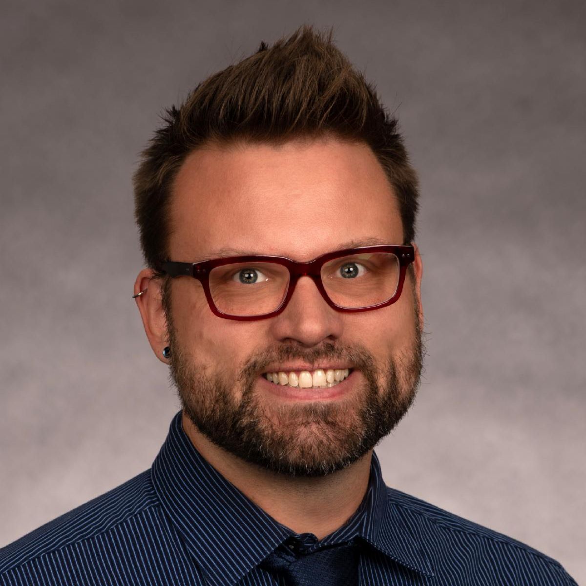 Headshot of Dr. Kammerer. He is wearing a dark blue button up shirt and a black tie and black glasses.