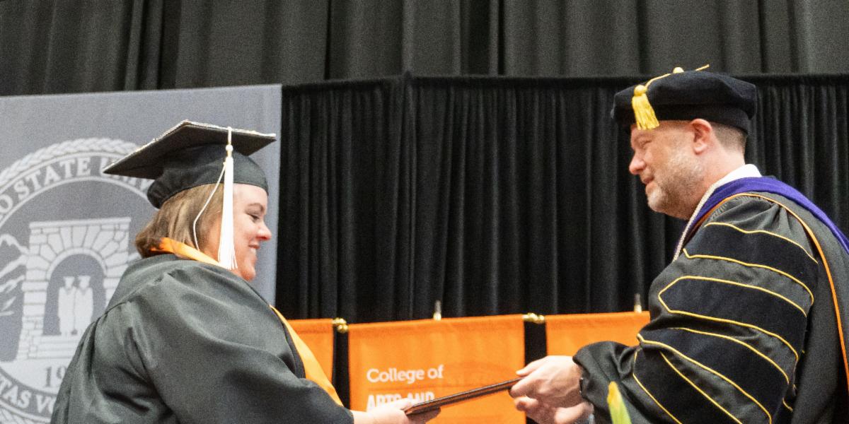 Carrie Page walks across commencement stage to accept diploma from Pres. Satterlee