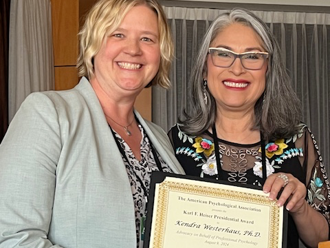Westerhaus smiles with another person at a podium, holding a certificate of her award