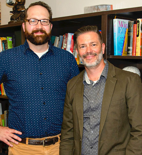 Professor Speer and Professor Dudgeon post together in front of a bookshelf, smiling.