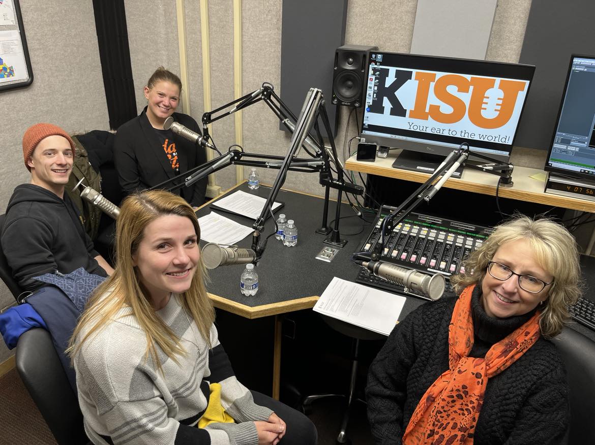 Tabitha LaForce, Noah Leary, Dani Mecham, Kandi Turley Ames pose for a photo together in the KISU recording studio. They are each sitting at a microphone with recording equipment behind them.