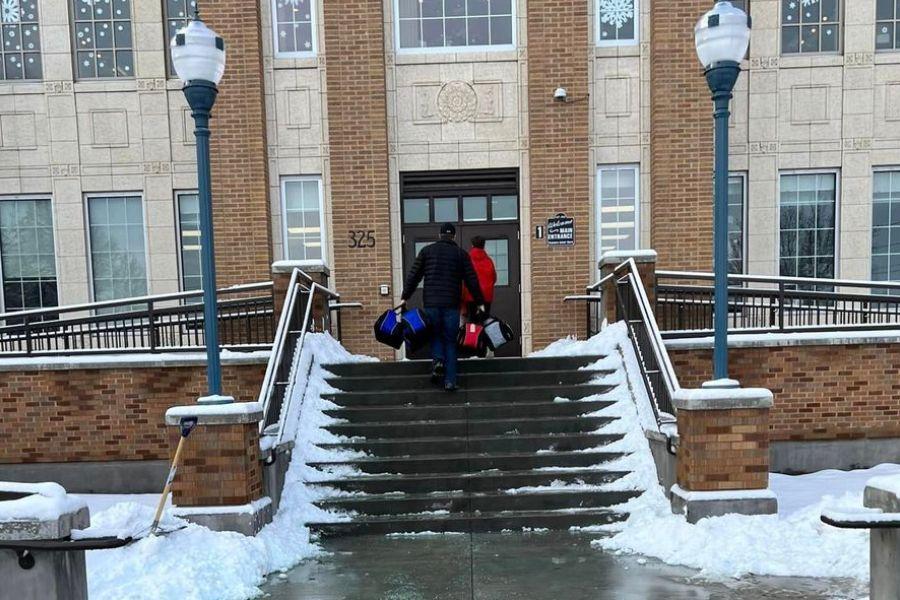 Volunteers deliver duffle bags for needy teens to Pocatello High School. They are walking up the snowy front stairs of the high school carrying the bags.