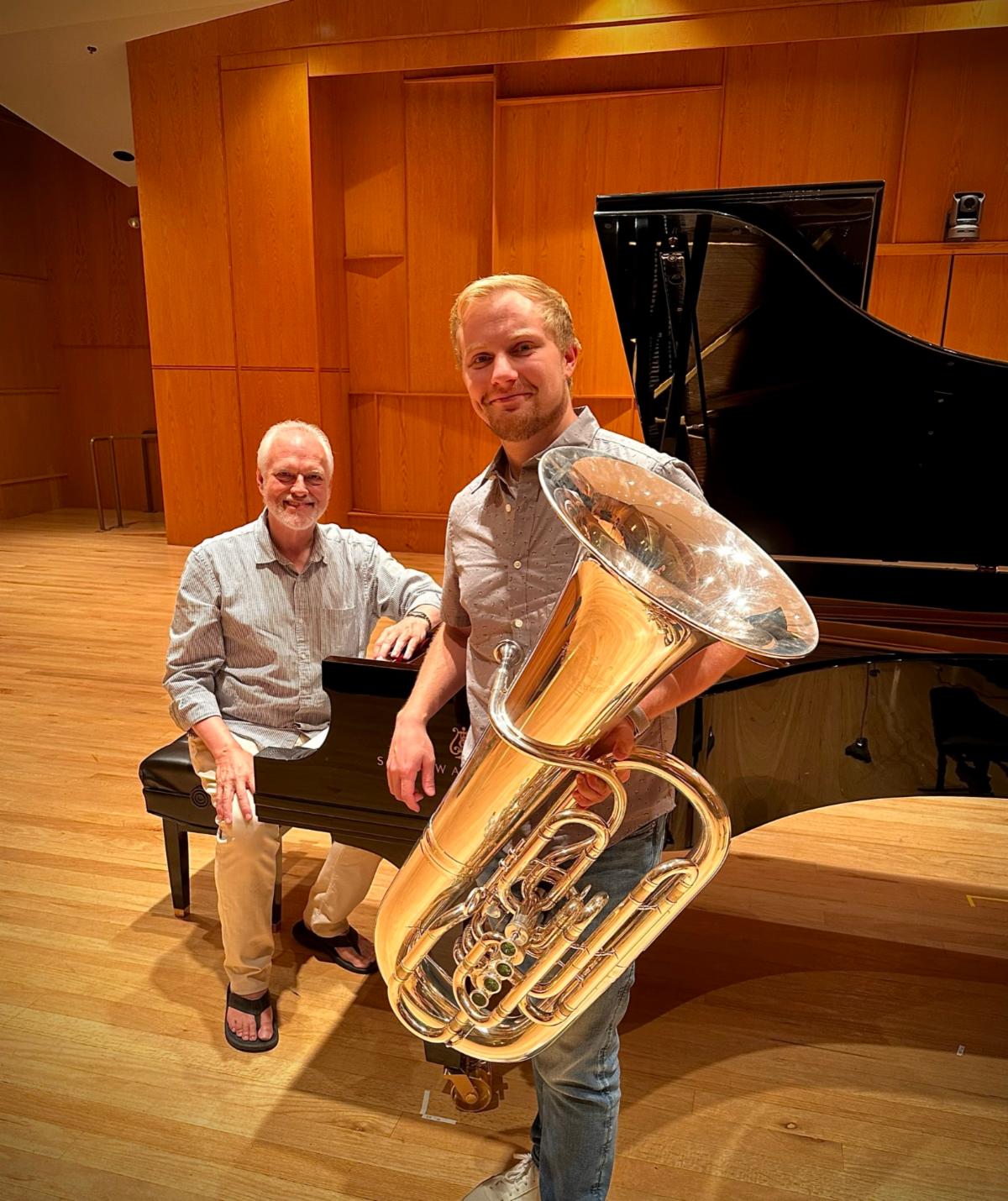 Neiwirth sits at a grand piano on a stage. Young stands next to it holding his tuba.