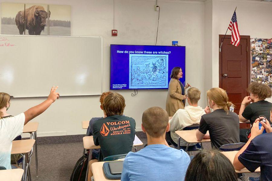 Marie Stango stands at the front of Pocatello High School classroom giving a presentation. Students in the class look at her. One student is raising his hand.