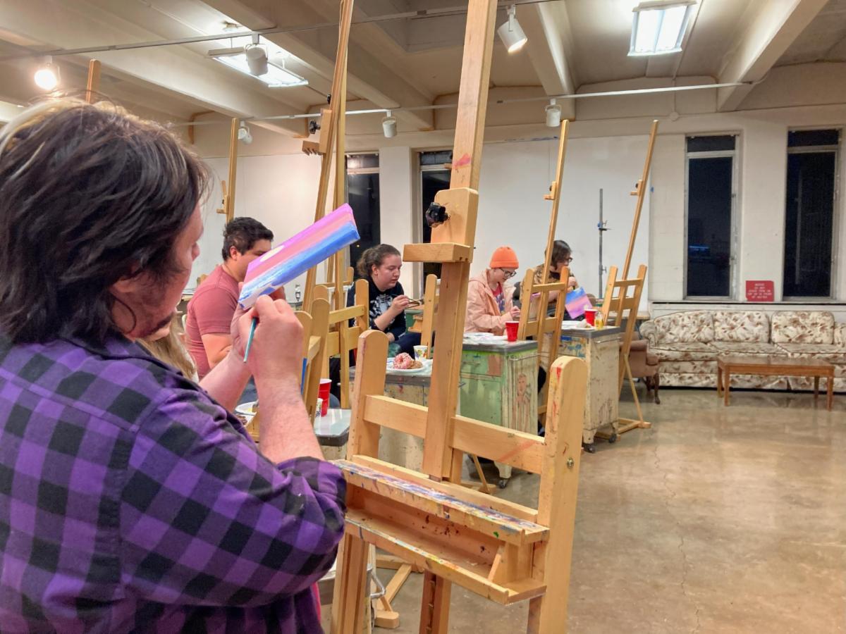  Art club members work in the art studio on easels painting small canvases.